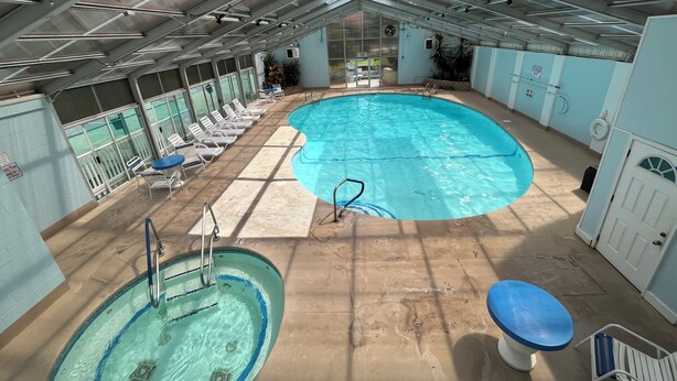 An indoor swimming pool with multiple lanes, lounge chairs, and a separate hot tub area.