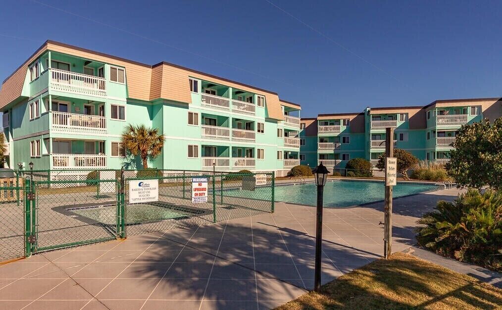 A multi-story hotel with balconies, a swimming pool, and a fenced area.