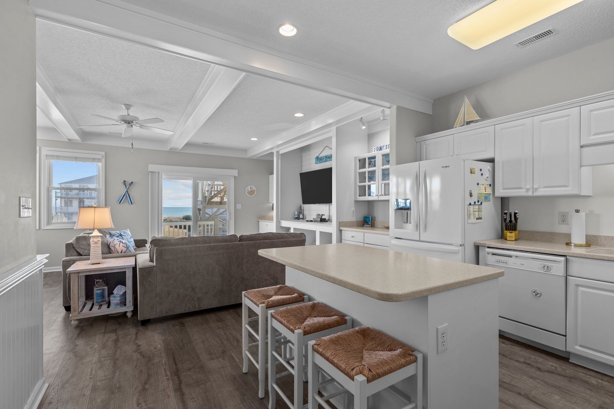 A modern kitchen with white cabinetry, a central island, and a dining area with a grey sofa and bar stools.