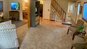 A living room with a television, a bookshelf, a staircase, and a dining area. - Cozy Cascade Retreat (Cascade)