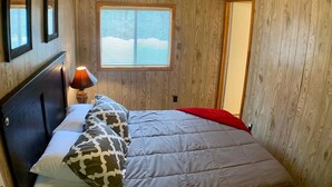A bedroom with a bed, a nightstand, a lamp, and a window with blinds. - Cozy Cascade Retreat (Cascade)