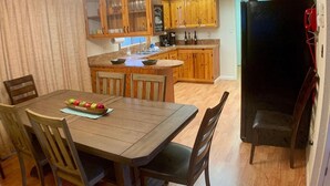 A kitchen with wooden cabinets, a dining table with chairs, and a refrigerator. - Cozy Cascade Retreat (Cascade)