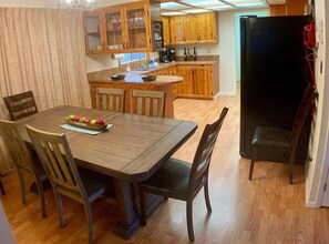 A kitchen with wooden cabinets, a dining table with chairs, and a refrigerator. - Cozy Cascade Retreat (Cascade)