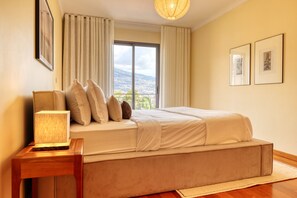 Une chambre à coucher avec un lit, une table de chevet, une lampe, une fenêtre avec des rideaux et des tableaux encadrés accrochés au mur.