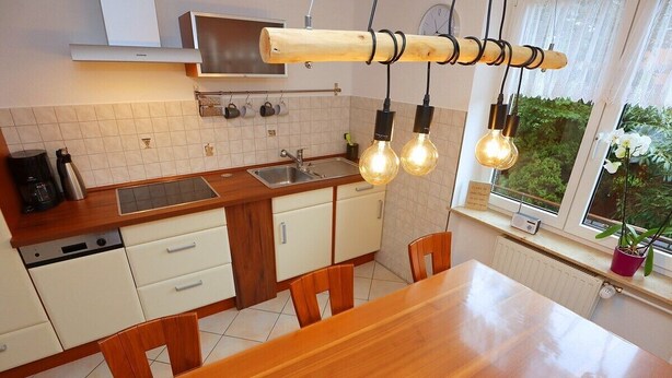 A modern kitchen with a wooden table and chairs, a built-in oven, and a window with a view of greenery. - Erdgeschoßwohnung 85qm (Villingen-Schwenningen)