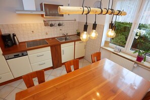 A modern kitchen with a wooden table and chairs, a built-in oven, and a window with a view of greenery. - Erdgeschoßwohnung 85qm (Villingen-Schwenningen)