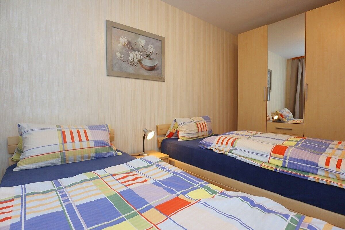 A hotel room with two beds, a nightstand, a lamp, a painting, and a mirror.