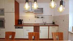 A compact kitchen with white cabinets, a wooden countertop, and a dining area with a table and chairs. There are three pendant lights hanging above the sink. - Erdgeschoßwohnung 85qm (Villingen-Schwenningen)
