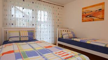 Un dormitorio con dos camas, una ventana con cortinas translúcidas y un cuadro en la pared.