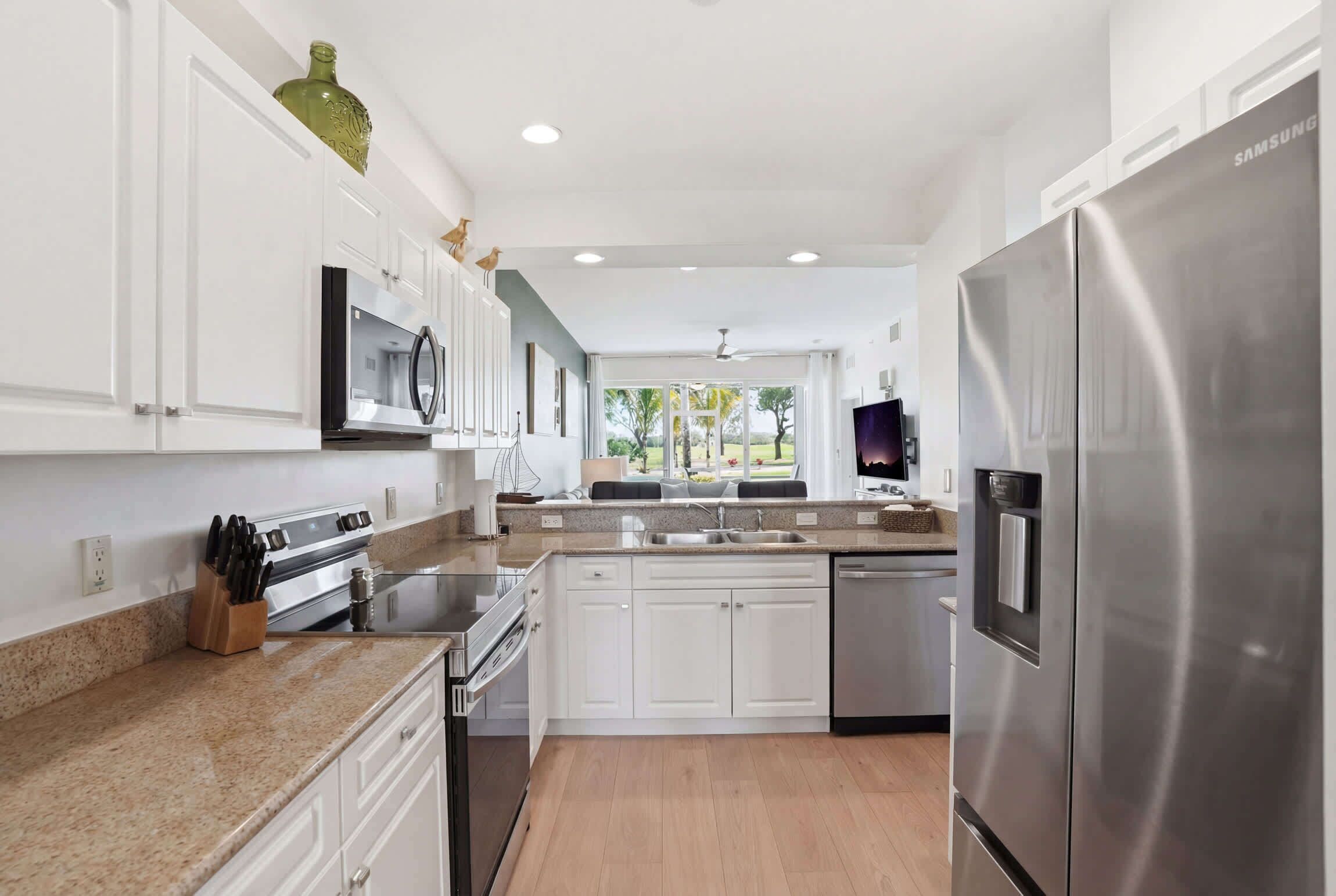 A modern kitchen with white cabinets, stainless steel appliances, a granite countertop, and a view of the outdoors.