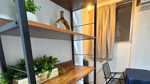 Ein Zimmer mit Holzboden, einem Metallregal mit Pflanzen, einem Tisch mit blauer Tischdecke und einem Fenster mit Vorhängen.