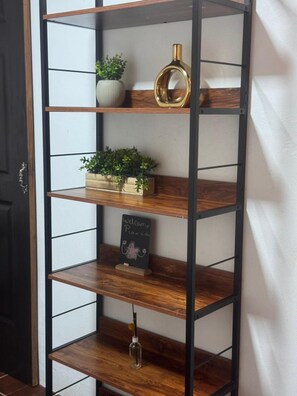 A metal shelving unit with multiple shelves, some holding plants and a chalkboard sign. - AC/WIFI/HOT WATER (La Fortuna)
