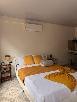 Habitación de hotel con cama, mesita de noche, lámpara, una pequeña mesa con una planta y aire acondicionado instalado en la pared.