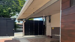 Un edificio con un acceso cubierto, un camino de entrada con puerta y un área pavimentada con un pequeño jardín.