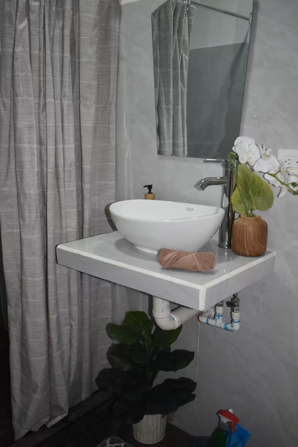 Een badkamer met een witte wastafel, een spiegel, een handdoek, een kamerplant en een douchegordijn.