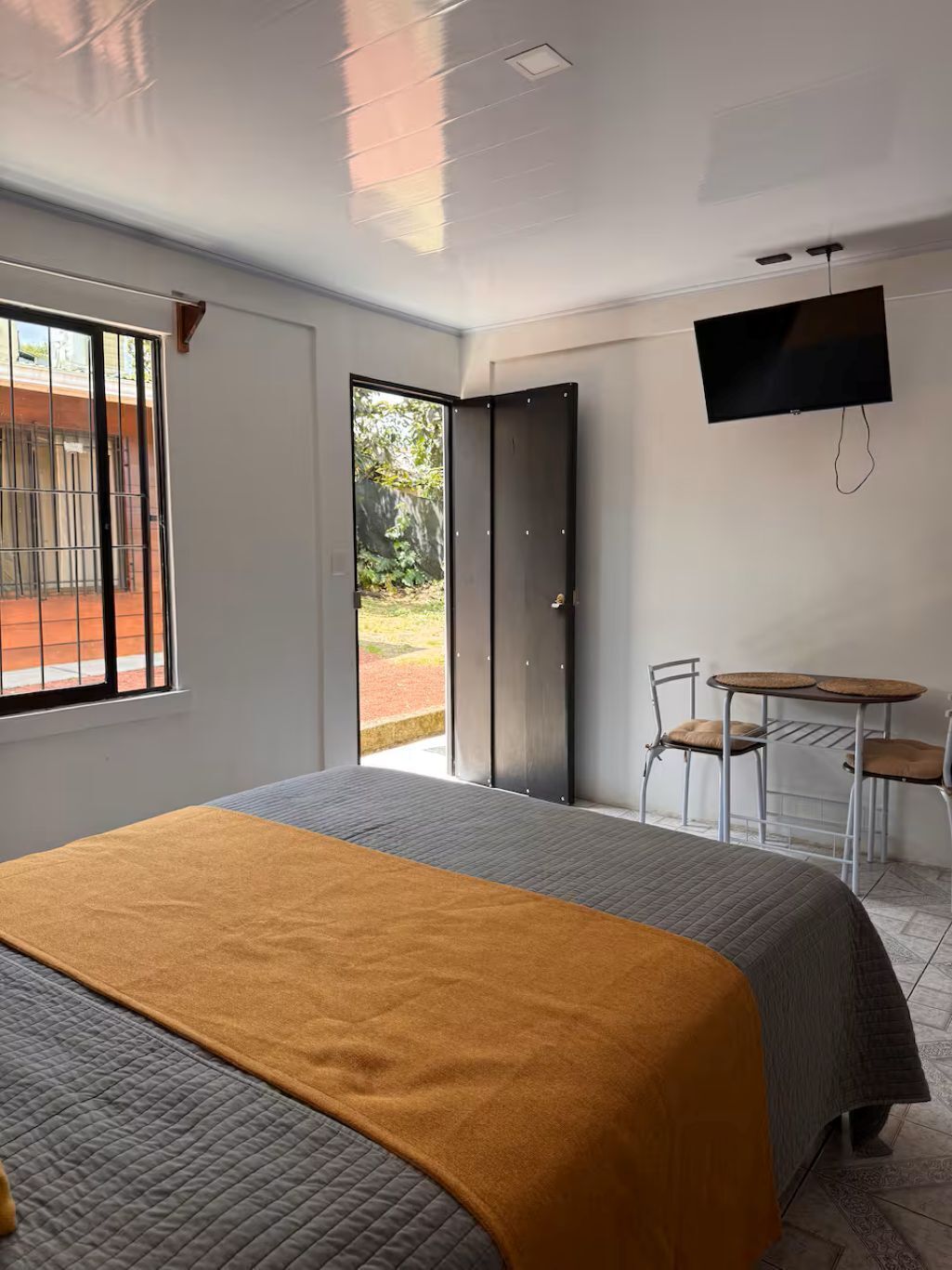 A modern hotel room with a bed, a TV, a small table, and chairs.