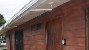 Un edificio con facciata in legno, una porta metallica, una piccola finestra e una telecamera di sicurezza.