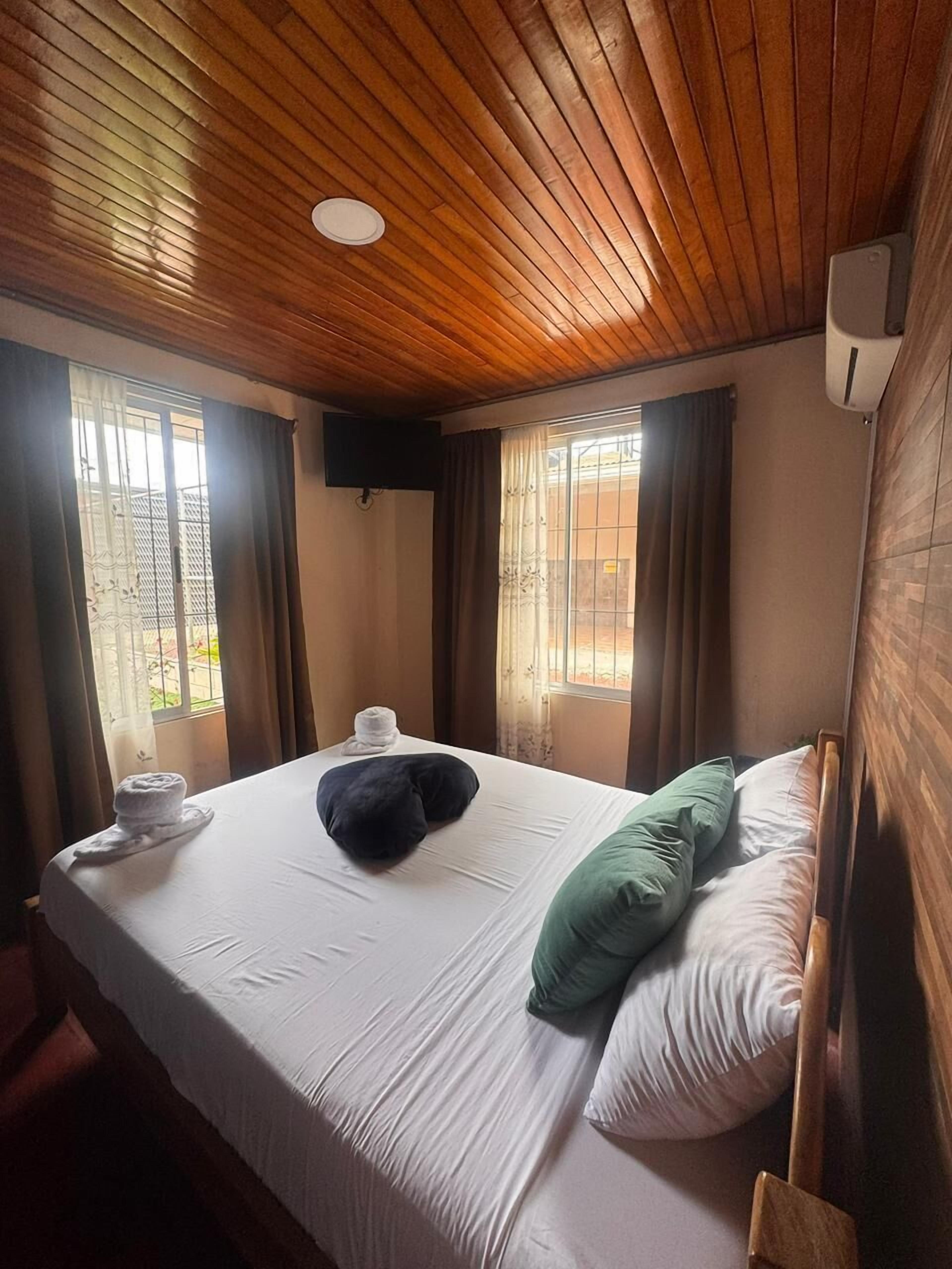 Una camera d'albergo con soffitto in legno, un letto con biancheria bianca, un cuscino verde, un cuscino bianco e un asciugamano sul letto.