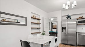 Une cuisine moderne avec un réfrigérateur en acier inoxydable, des étagères en bois et une table à manger blanche avec des chaises.
