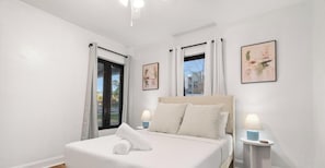 Une chambre d’hôtel comprenant un lit, deux tables de chevet avec des lampes, une fenêtre avec des rideaux et deux tableaux encadrés accrochés au mur.