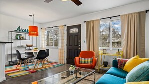 A living room with a sofa, chairs, a coffee table, a dining area with a table and chairs, a bookshelf, and a door. - Stylish 1BR/1BA SoCo Condo | Skyline Views, Pool & Parking by Austin Vacay (Austin)