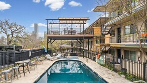 A swimming pool with lounge chairs and a covered seating area, surrounded by a fenced patio. - Stylish 1BR/1BA SoCo Condo | Skyline Views, Pool & Parking by Austin Vacay (Austin)