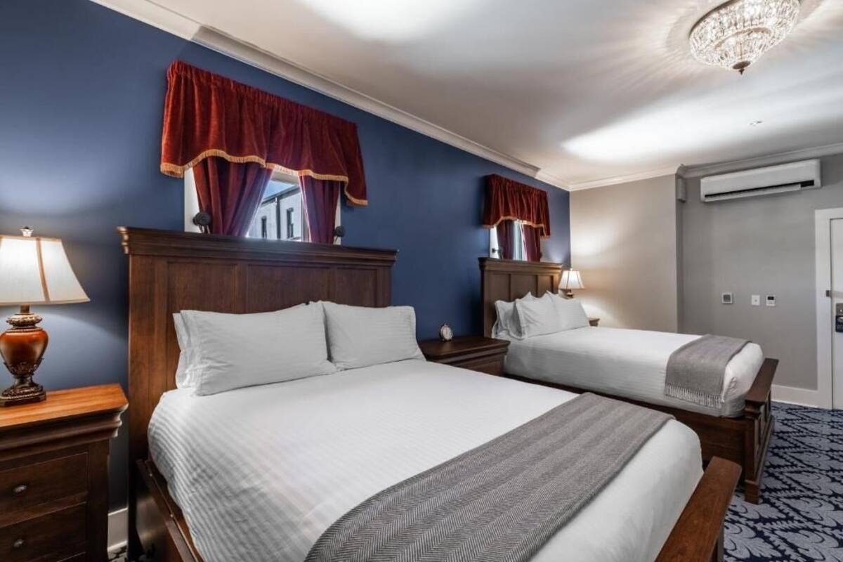 Habitación de hotel con dos camas, un cabecero de madera, una araña y una alfombra estampada.