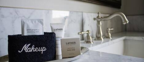 A bathroom vanity with a mirror, a sink, and toiletries including a black towel labeled 'Makeup,' a cleansing cloth, and Lather body soap.