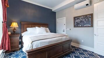 A bedroom with a wooden bed, a nightstand with a lamp, a patterned carpet, and a framed picture on the wall.