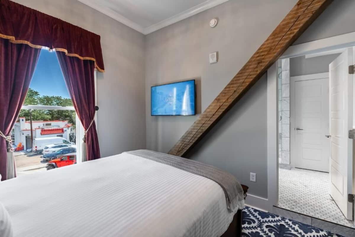 Habitación de hotel con cama, televisión, vista al exterior y puerta que da a otra habitación.