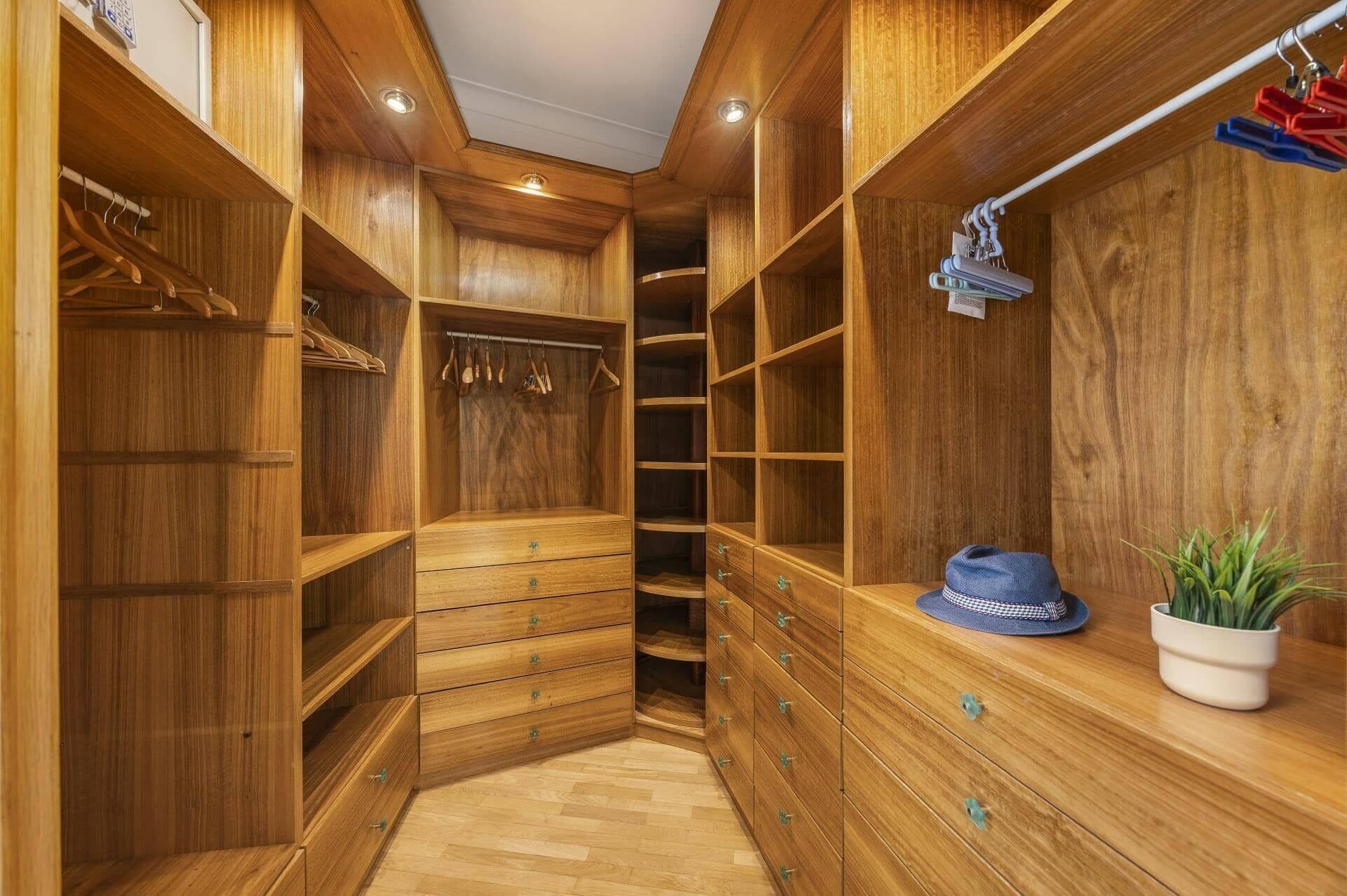 A wooden walk-in closet with multiple shelves, drawers, and hanging space.