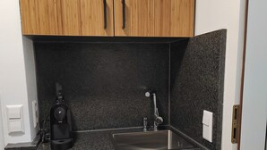 A compact kitchen with wooden cabinets, a granite countertop, a coffee maker, and a stainless steel sink. - Room 116 at the AlbThermen (Bad Urach)