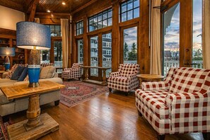 A spacious room with large windows, a checkered sofa, a wooden coffee table, and a lamp.