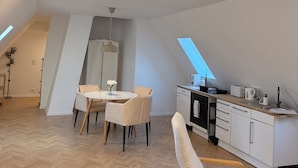 En modern lägenhet i loftstil med matplats, kök och ett stort fönster som släpper in naturligt ljus.