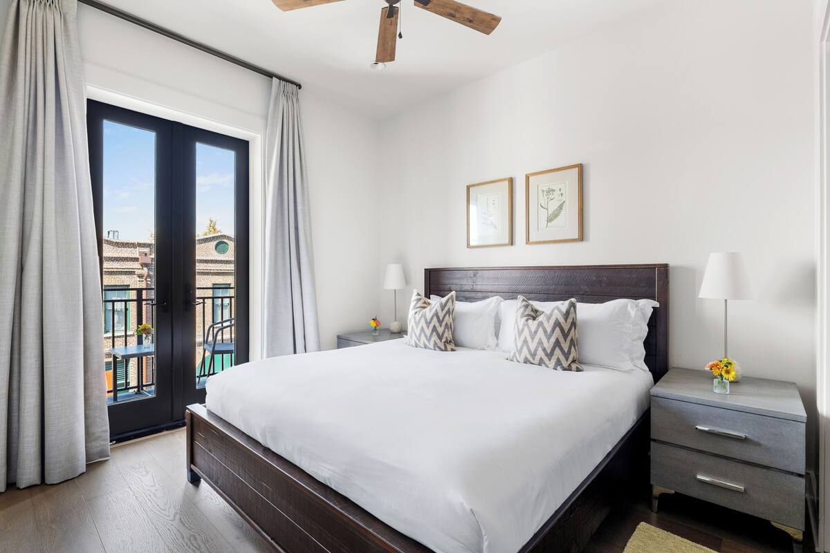 A hotel room with a large bed, two bedside tables, a ceiling fan, and a view of the outside.