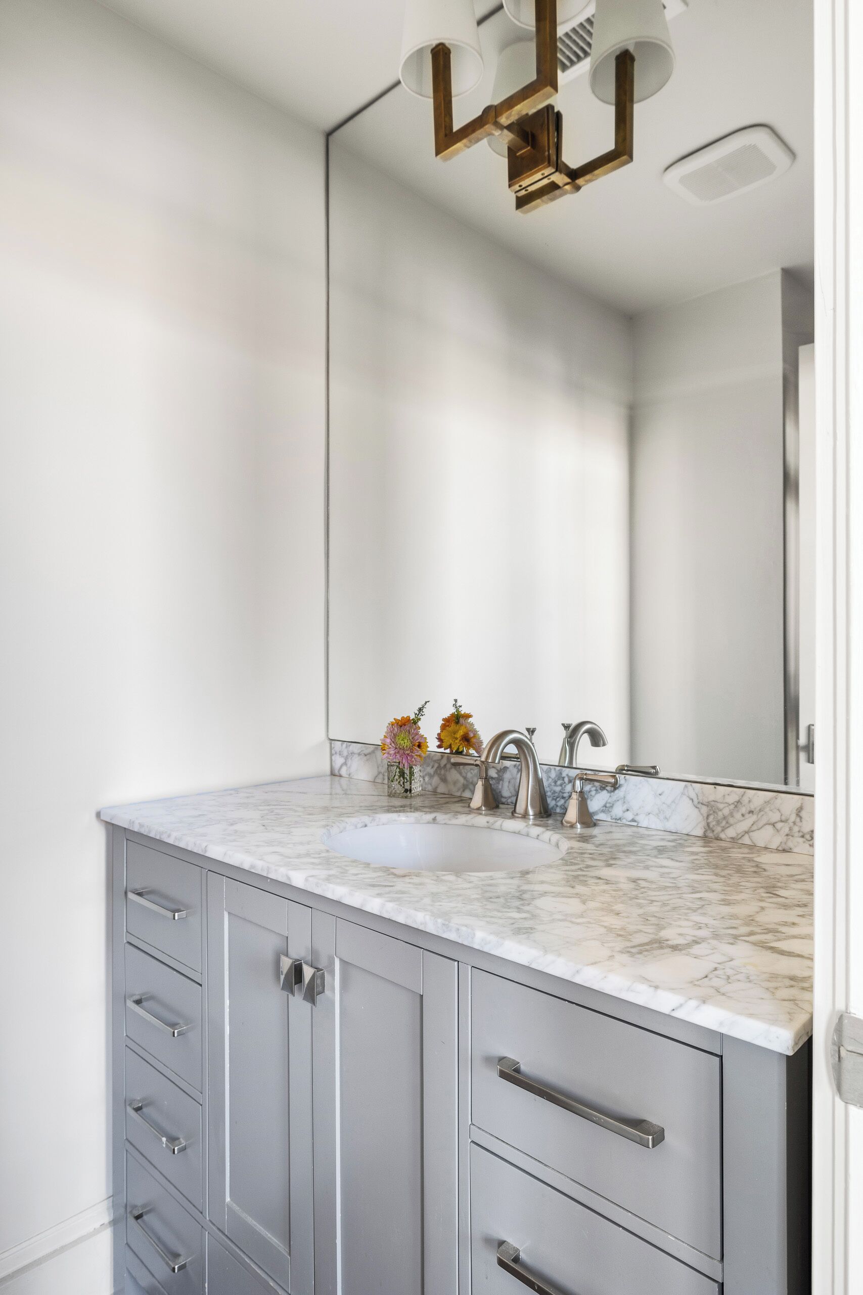 A bathroom with a marble sink, two faucets, a mirror, and a modern light fixture.