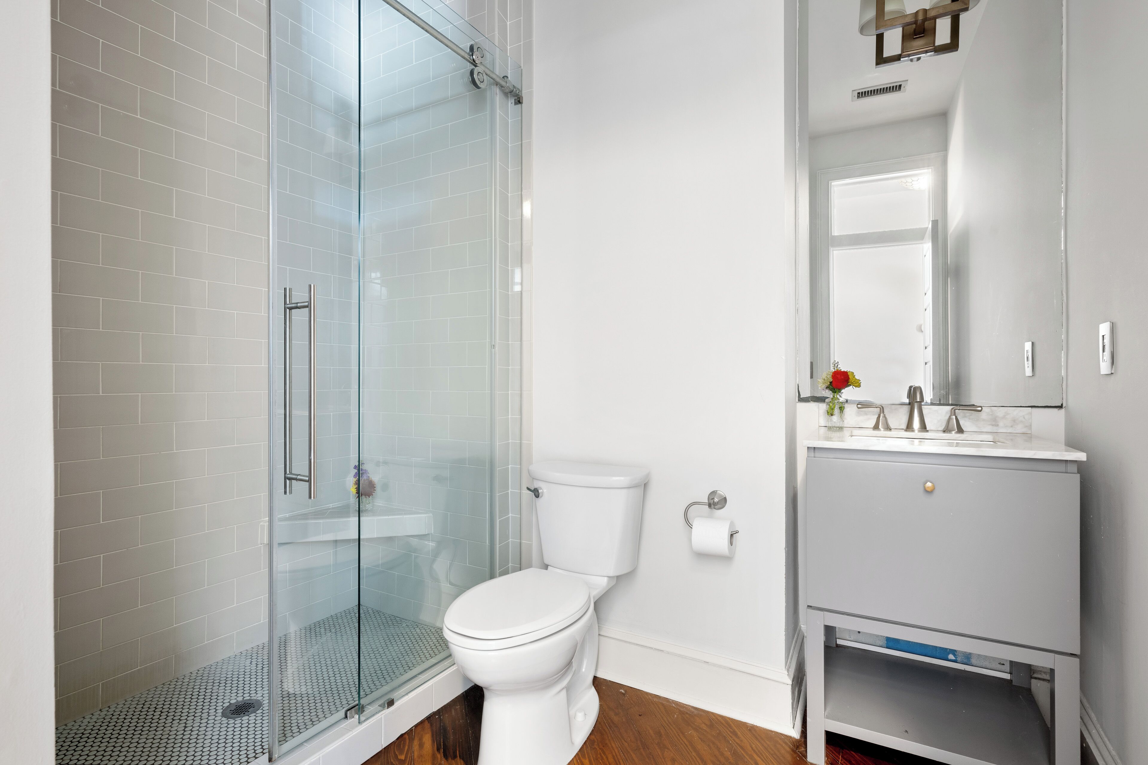 Un baño con cabina de ducha de vidrio, inodoro blanco y tocador gris con espejo.