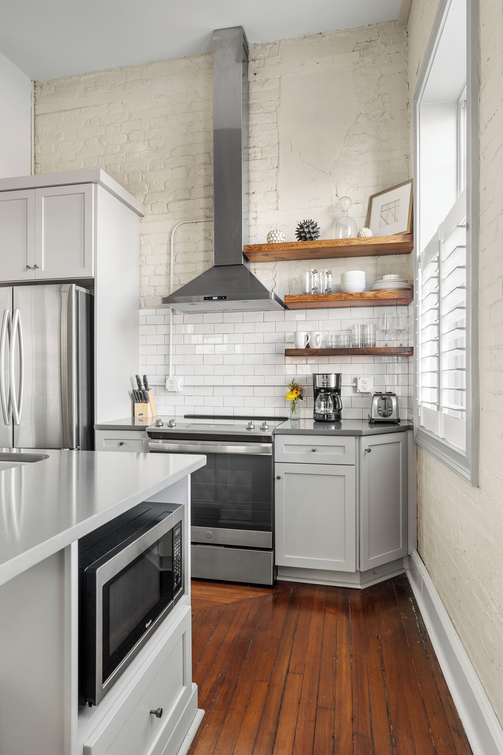 A modern kitchen with white cabinetry, stainless steel appliances, and a brick wall.