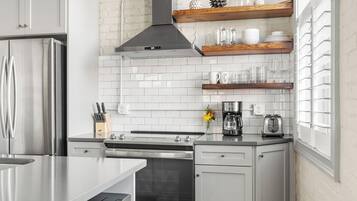 A modern kitchen with white cabinetry, stainless steel appliances, and a brick wall.