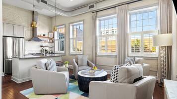 A modern living room with a kitchen, large windows, and a ceiling fan.
