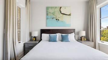 A hotel room with a large bed, two bedside tables with lamps, a wall-mounted artwork, and a window with curtains.