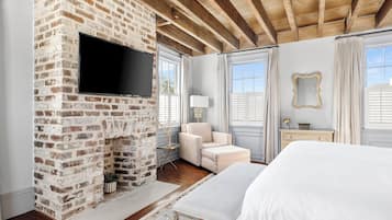 A bedroom with a brick fireplace, a bed, a TV, and a window with curtains.