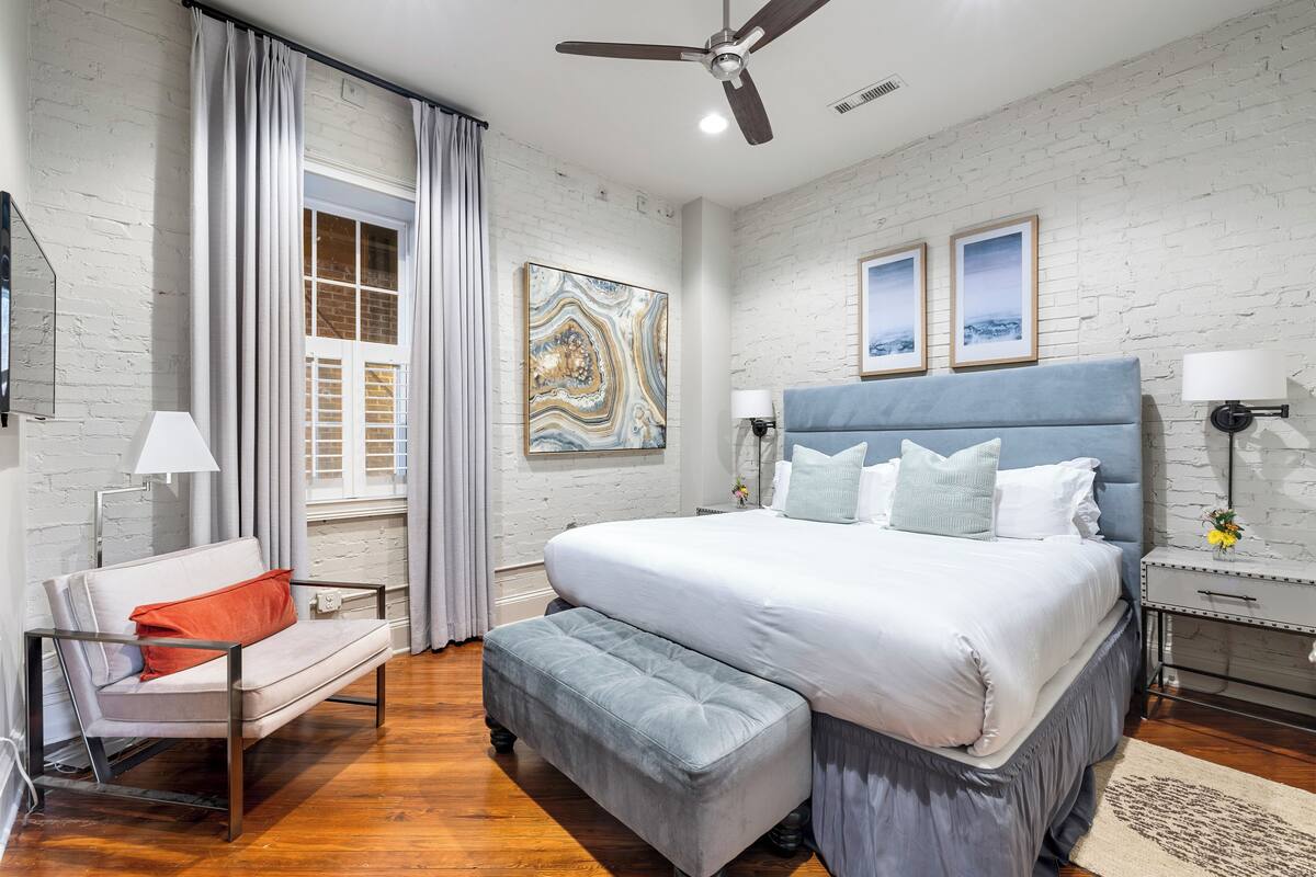 A bedroom with a large bed, a sofa, a ceiling fan, and a window with curtains.