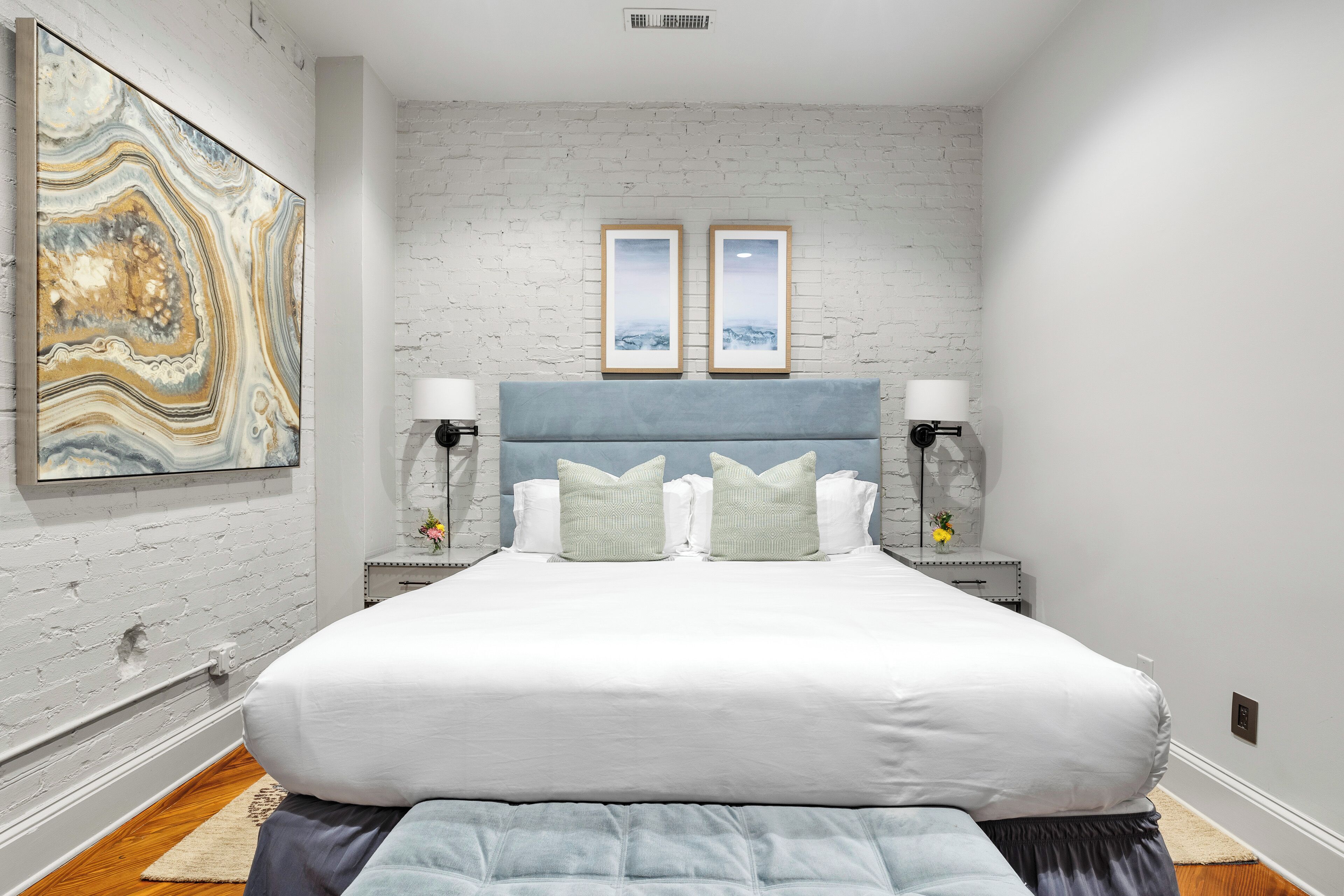 Een slaapkamer met een bed, twee nachtkastjes, een hoofdeinde en een aan de muur hangend kunstwerk.