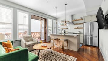 A modern kitchen with a stainless steel refrigerator, a bar area, and a seating area with a green sofa and a round coffee table.