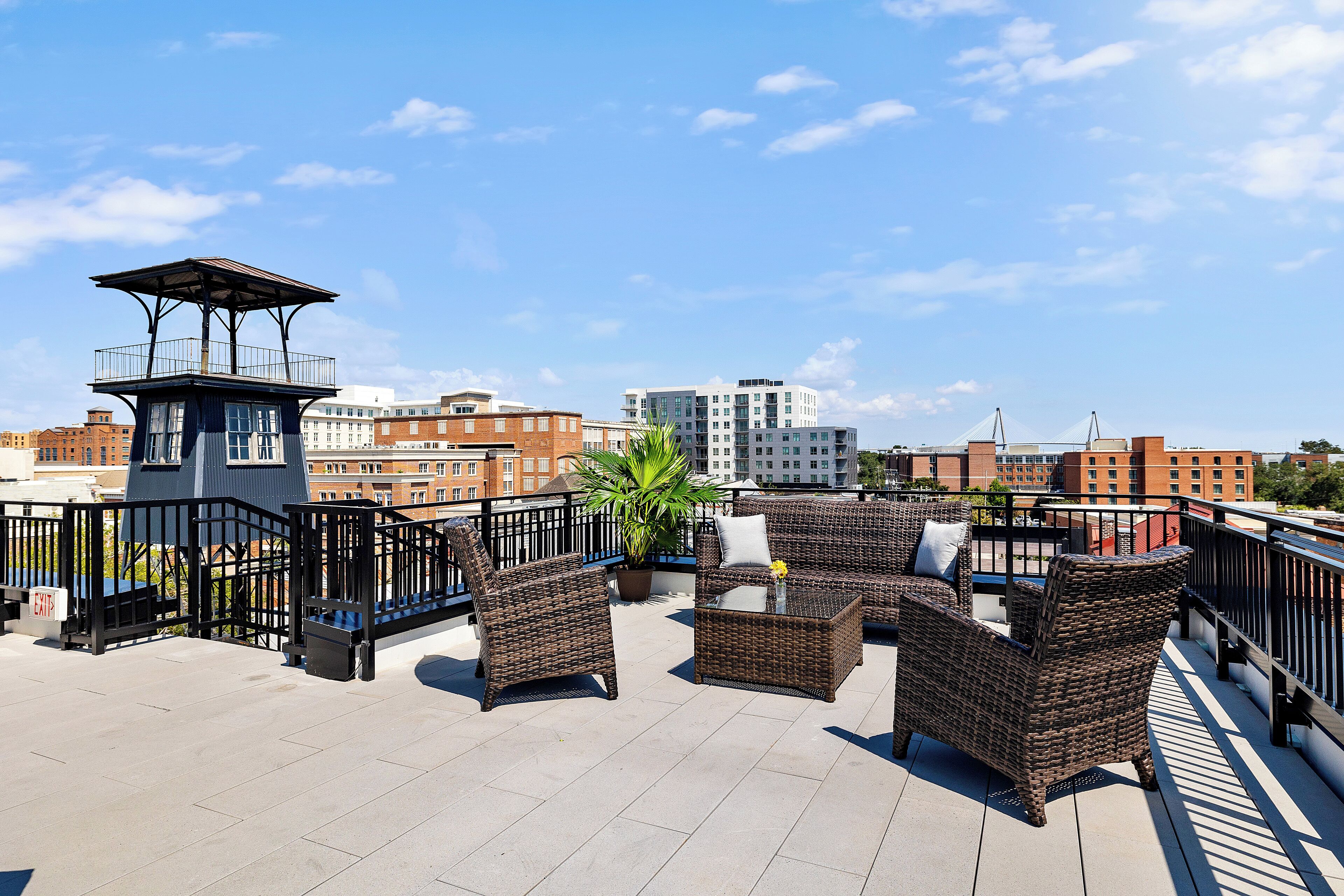 A rooftop terrace with wicker furniture, a small table, and a potted plant.