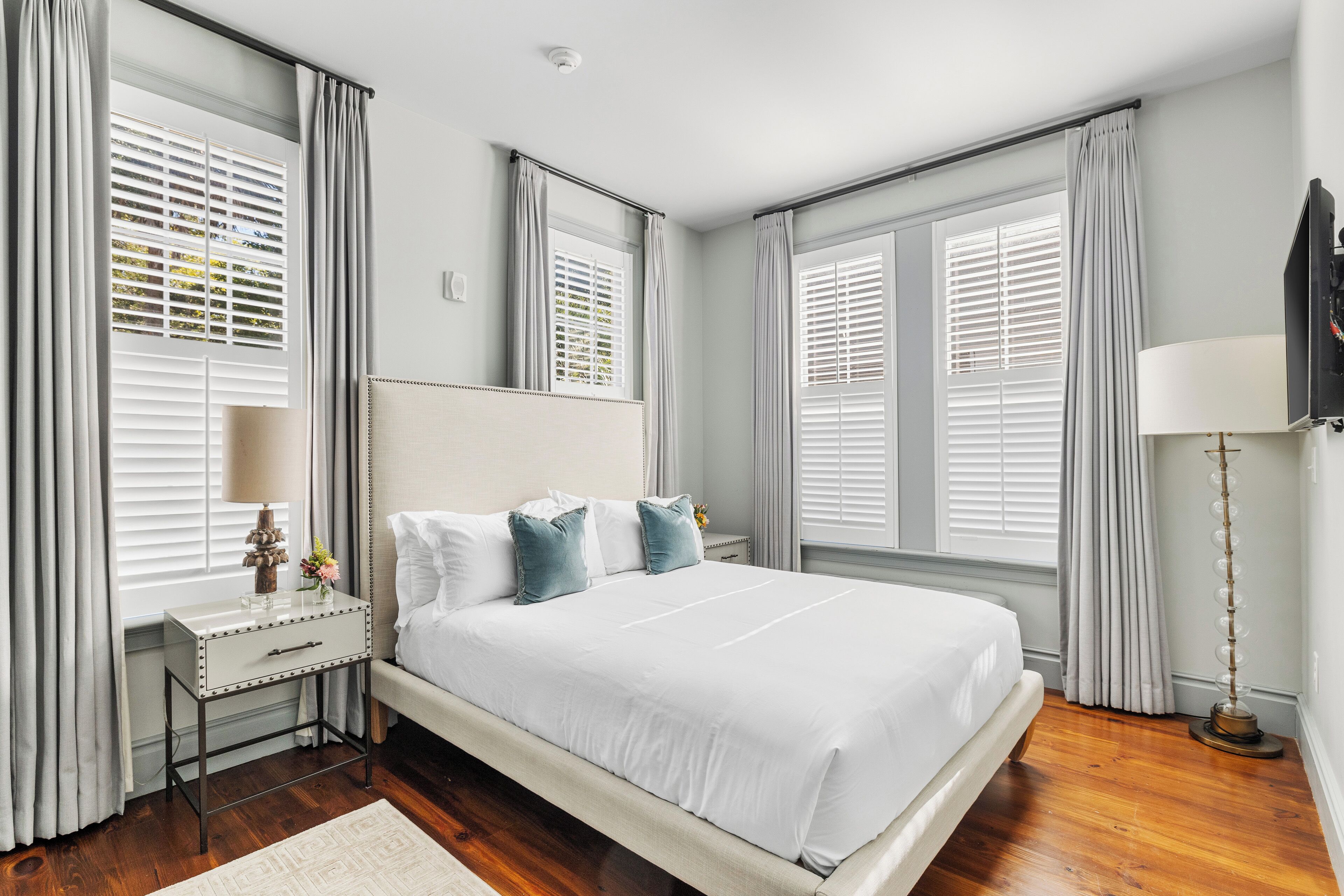 A bedroom with a large bed, a bedside table with a lamp, a nightstand, and a mirror.