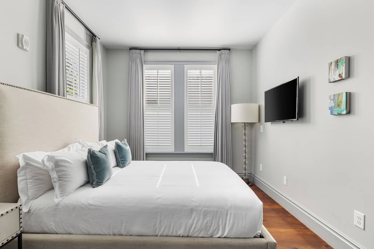 A bedroom with a bed, curtains, a TV, and artwork on the wall.