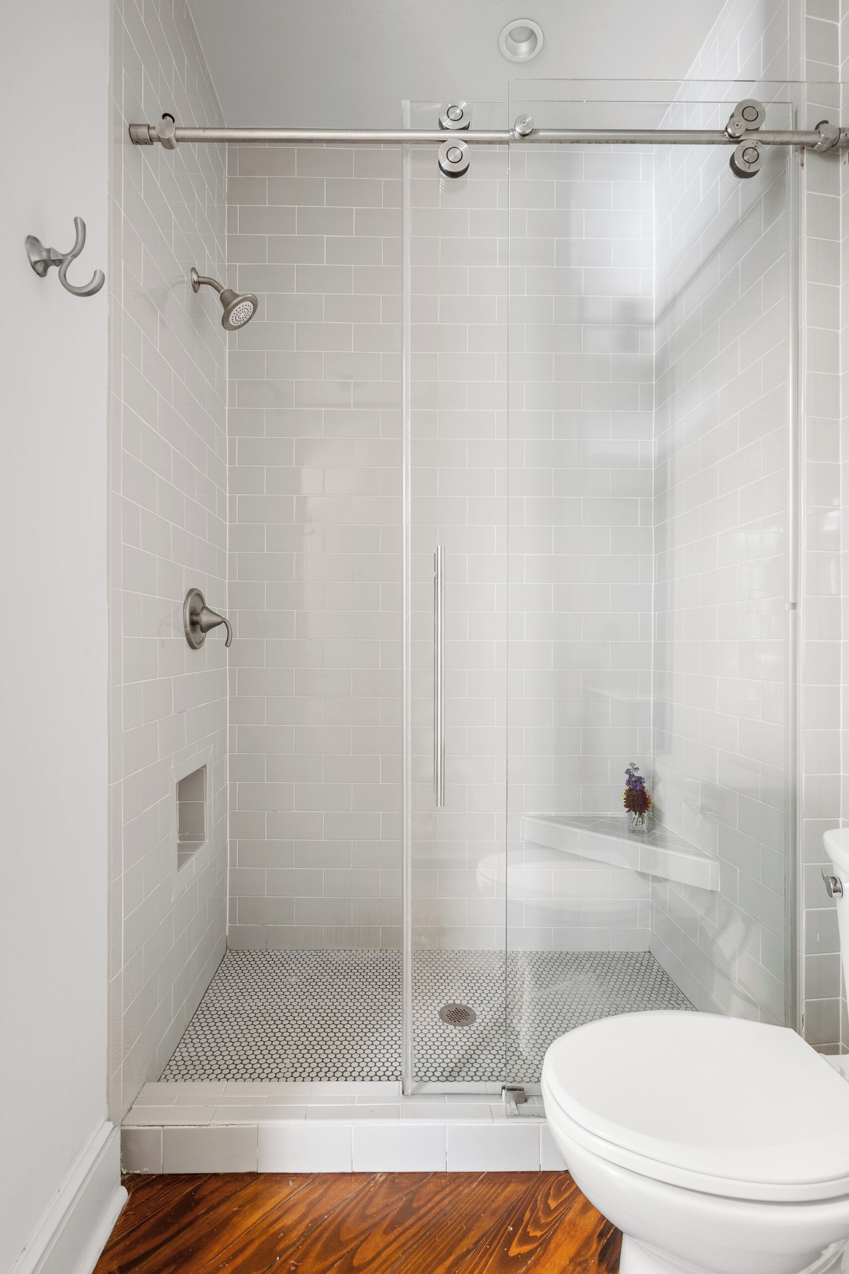 A shower with a glass door, a white toilet, and a wooden floor.