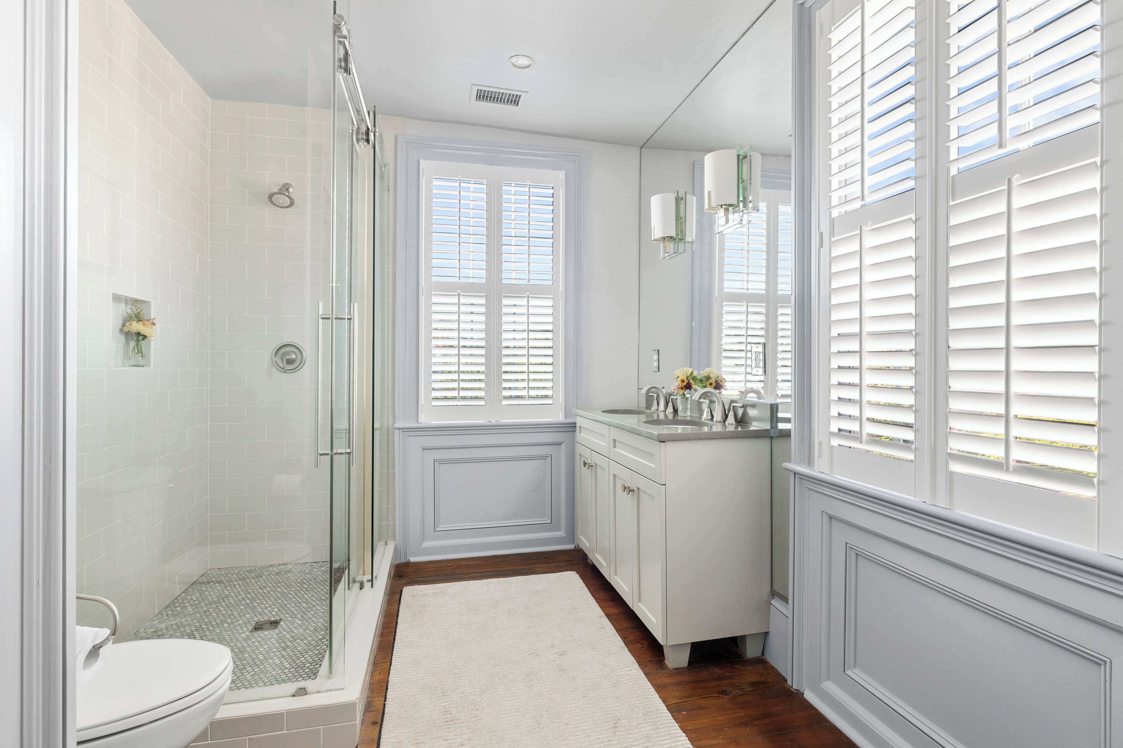 A bathroom with a shower, toilet, vanity, and large windows.